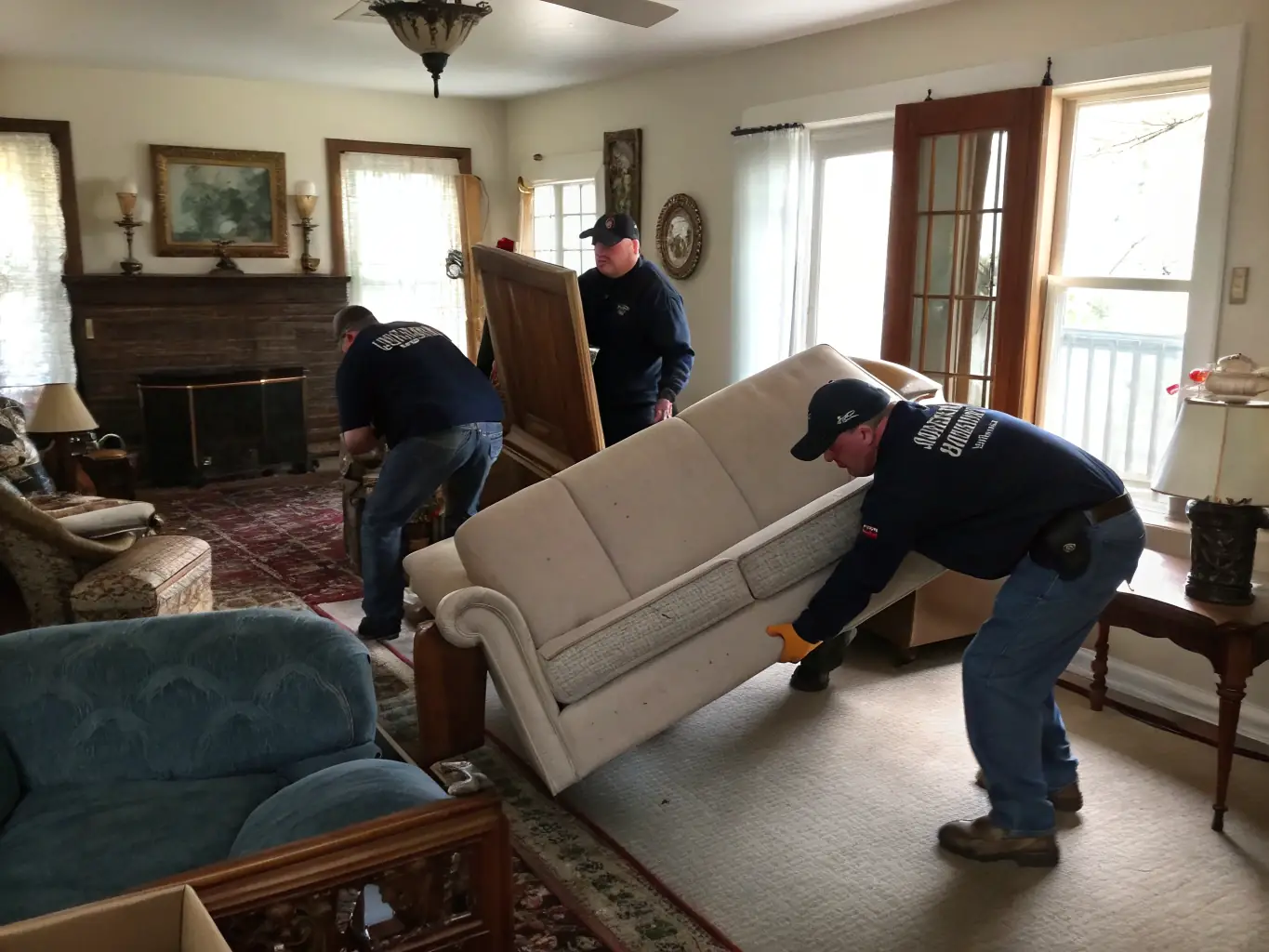 A professional team from Cleansoul LLC is carefully removing old furniture from a residential home, showcasing their junk removal service. The team is wearing branded uniforms and using protective equipment.